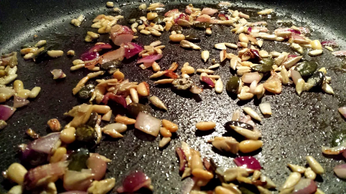  Zwiebelstücke und Kerne in der sesamgeölten Pfanne 