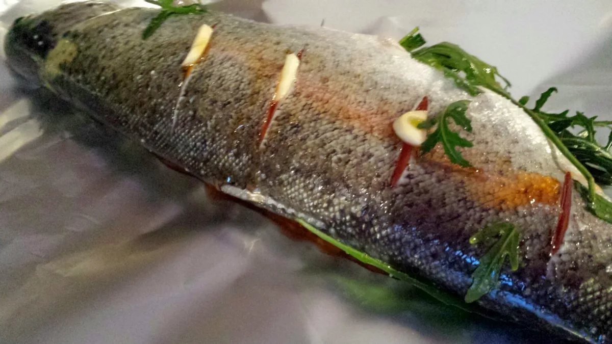 Forelle, gespickt mit Knoblauch, mit Chiliöl bestrichen, und mit Rukola gefüllt