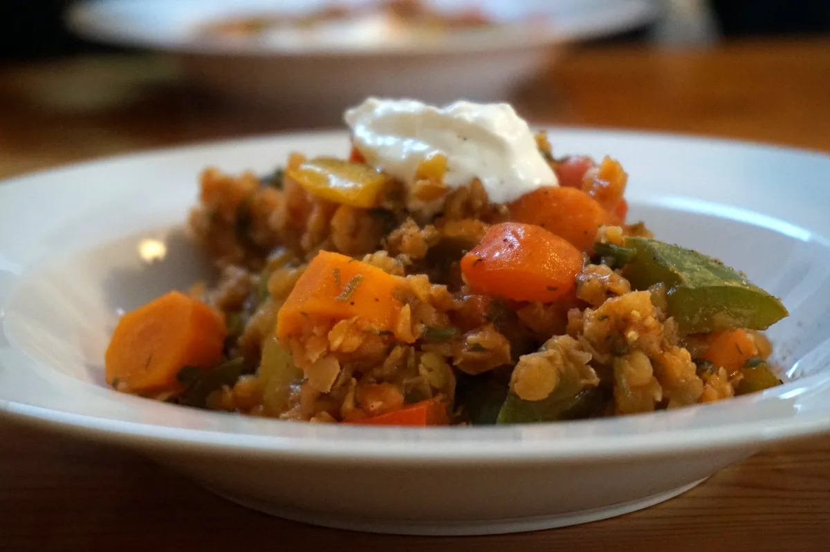 Ich fahre für ein paar Tage weg, darum musste das Gemüsefach im Kühlschrank geräumt werden. Viel war eh nicht mehr drin, nur ein paar Paprika, paar Karotten, ein Stück Ingwer, ein kleiner Bund Petersilie und ein kleiner Bund Dill. Eine Zwiebel und rote Linsen waren noch im Vorratsregal.  Die Zwiebel habe ich in der Pfanne angeschwitzt, die grob geschnittenen Paprika, Karotten und Ingwer mit dazu und die nur grob gehackte Petersilien und Dill -- einschließlich der Stengel -- dann auch mit rein. Dazu zwei Esslöffel Tomatenmark und ein wenig Wasser, Salz und Pfeffer. Das Gemüse habe ich dann bei kleiner Hitze schmurgeln lassen. Parallel dazu hab ich rote Linsen gekocht, sie dann abgegossen und zu dem Gemüse gegeben.  Beim Servieren kommt noch ein Klecks saurer Sahne obendrauf -- Veganer können die natürlich weglassen.  Nun kann ich beruhigt und satt wegfahren ...  Paprika und Karotten mit roten Linsen - und einen Klecks sauerer Sahne Paprika, Karotten, Ingwer, rote Linsen - und einen Klecks sauerer Sahne