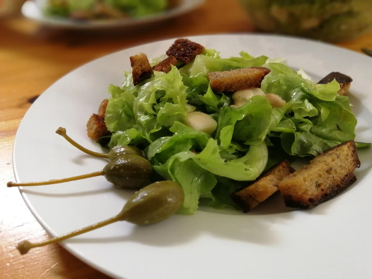 Salat mit warmen Croutons, Gorgonzolawürfeln und Kapernäpfeln.