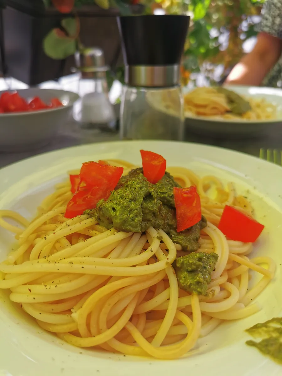 Spaghetti mit Tomaten und Pesto. Der Grünstich des Fotos kommt vom Sonnenschirm darüber.